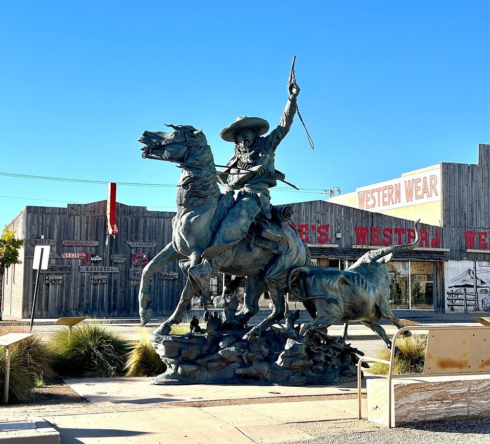 Bronze vaquero and longhorn sculpture on Main Street in downtown Artesia, NM, with western wear storefronts behind