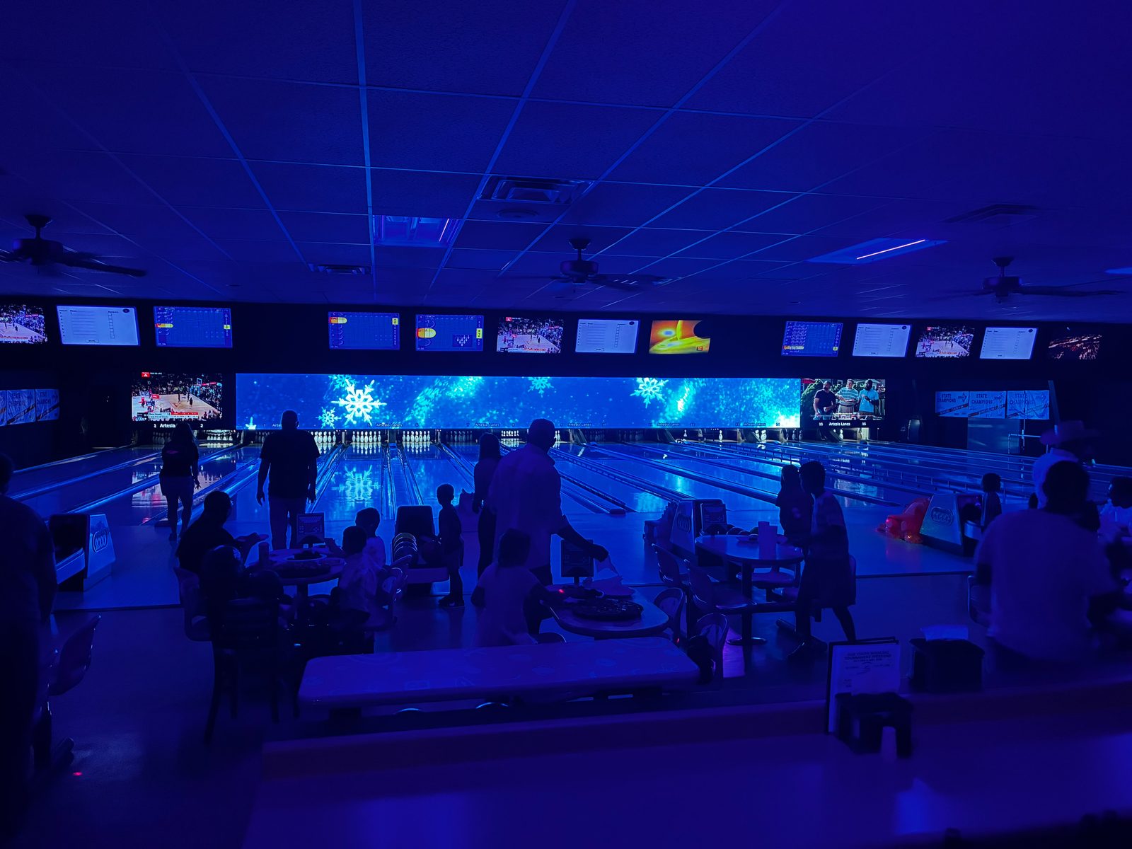 Glow bowling night at Artesia Lanes — lanes lit in blue under the LED media wall with families bowling